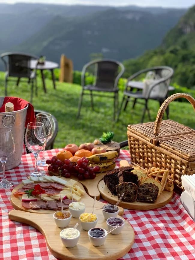 Piquenique com frutas, queijos e cesta de vime diante das montanhas em Olivas de Gramado